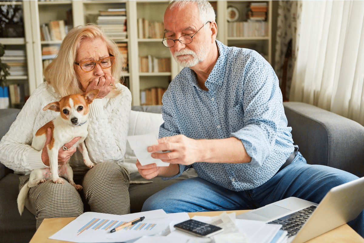 Older couple with small dog on couch reviewing financial documents