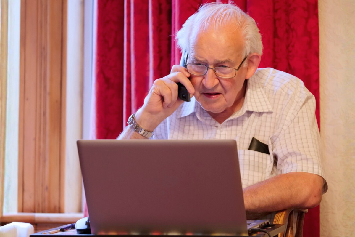 Older man on the phone sitting in front of his laptop computer