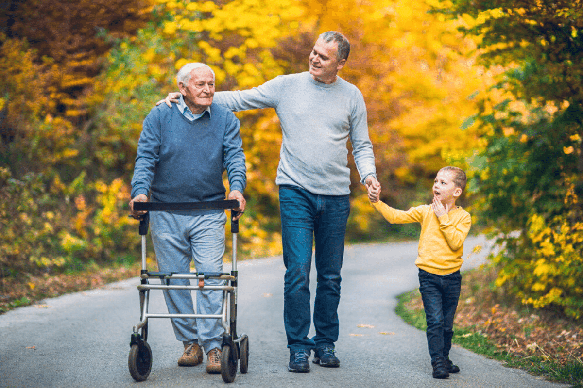 father, son, and grandfather in a walker take a stroll down a tree lined path