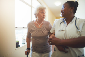 an older adult escorted down hallway by smiling nurse