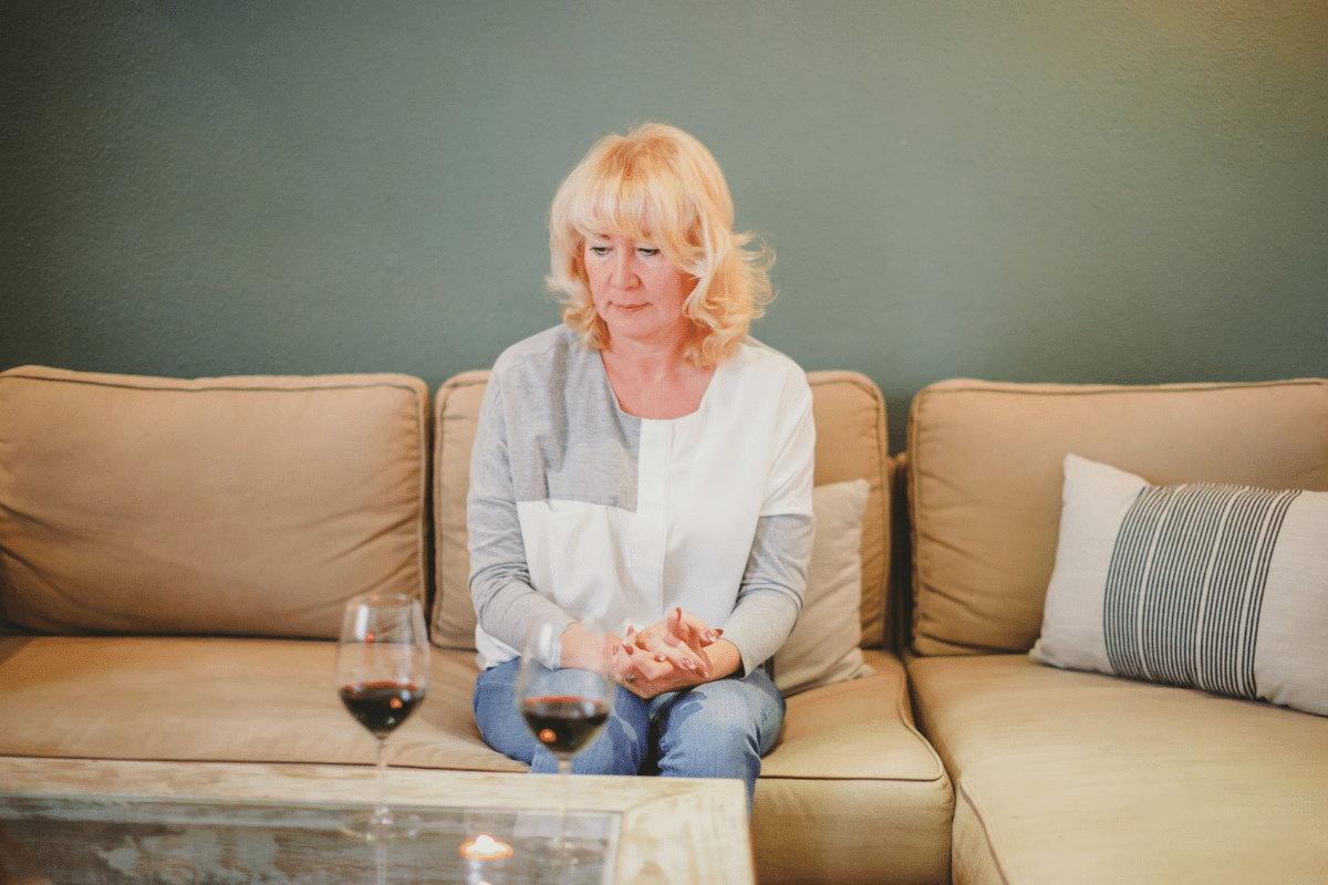 Sad woman sitting alone on a couch before a coffee table with two glasses of red wine