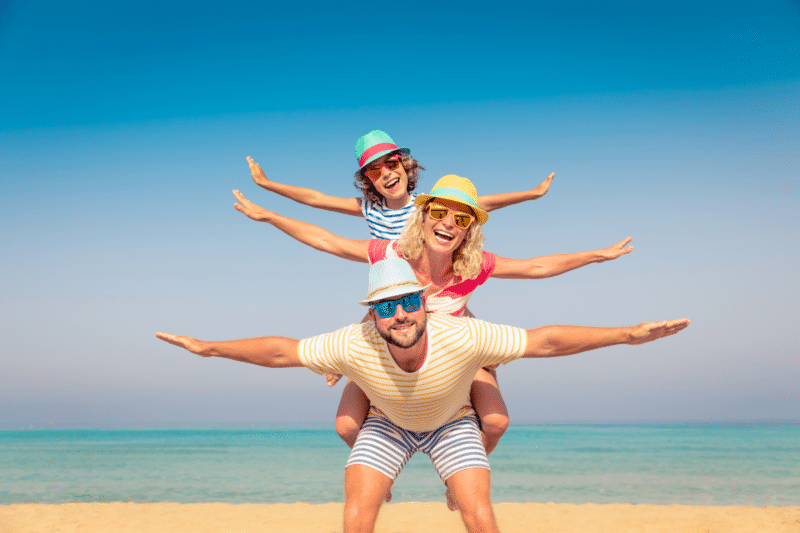 father, mother, and child play piggy back on a beach with open arms