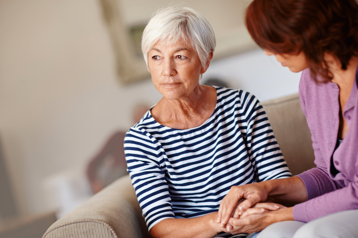 An older woman sitting on the couch, holding hands with another woman.