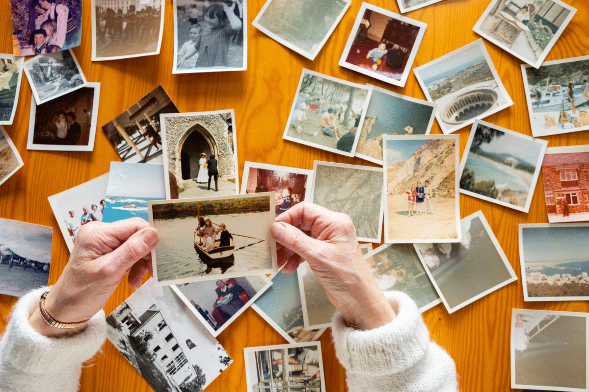Two hands holding a photo above a bunch of photos scattered across a table