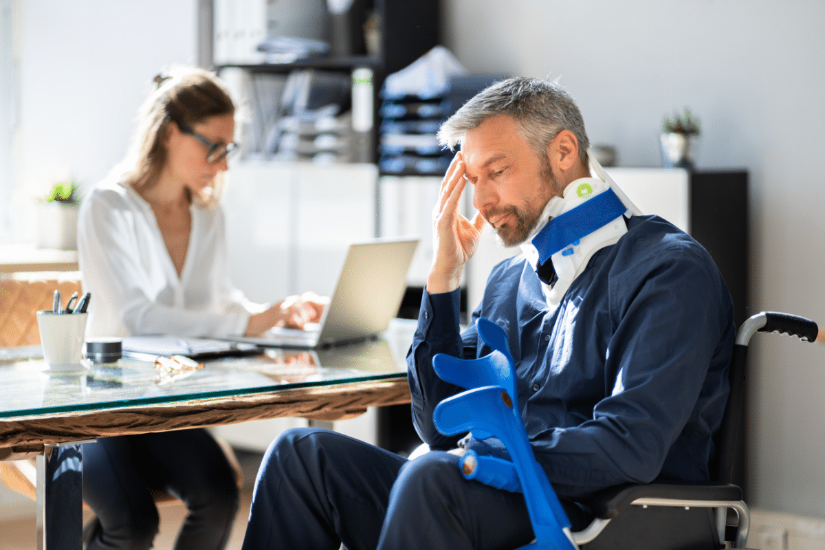 Injured man in neck brace and wheel chair sits in front of attorney at desk
