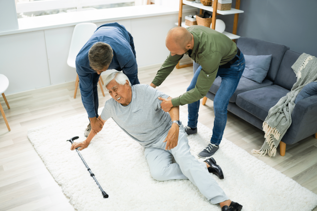 two men help an older man who has fallen to the floor with his cane