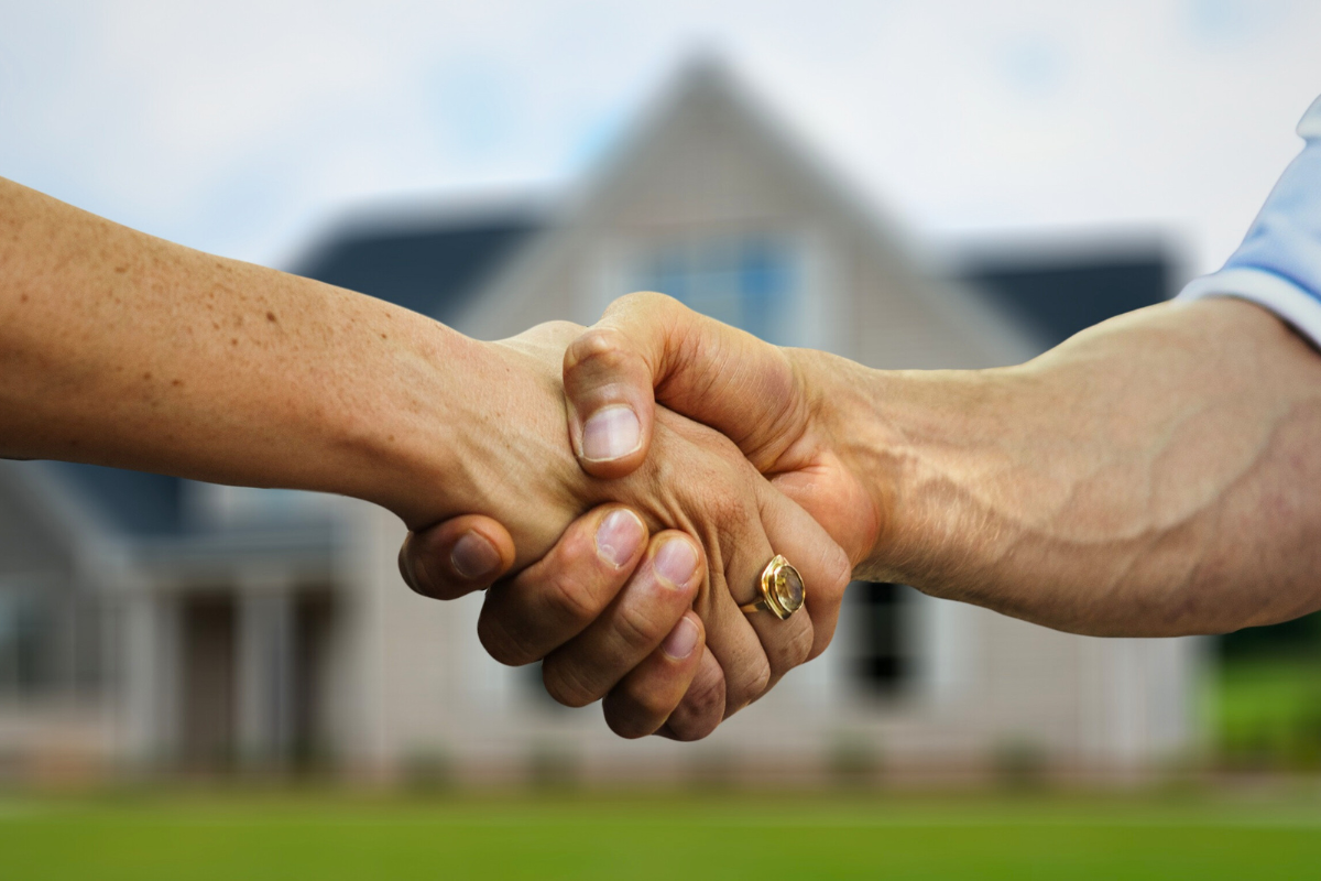 Hands shake in front of a residential home