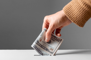 A hand putting money into a donation slot.