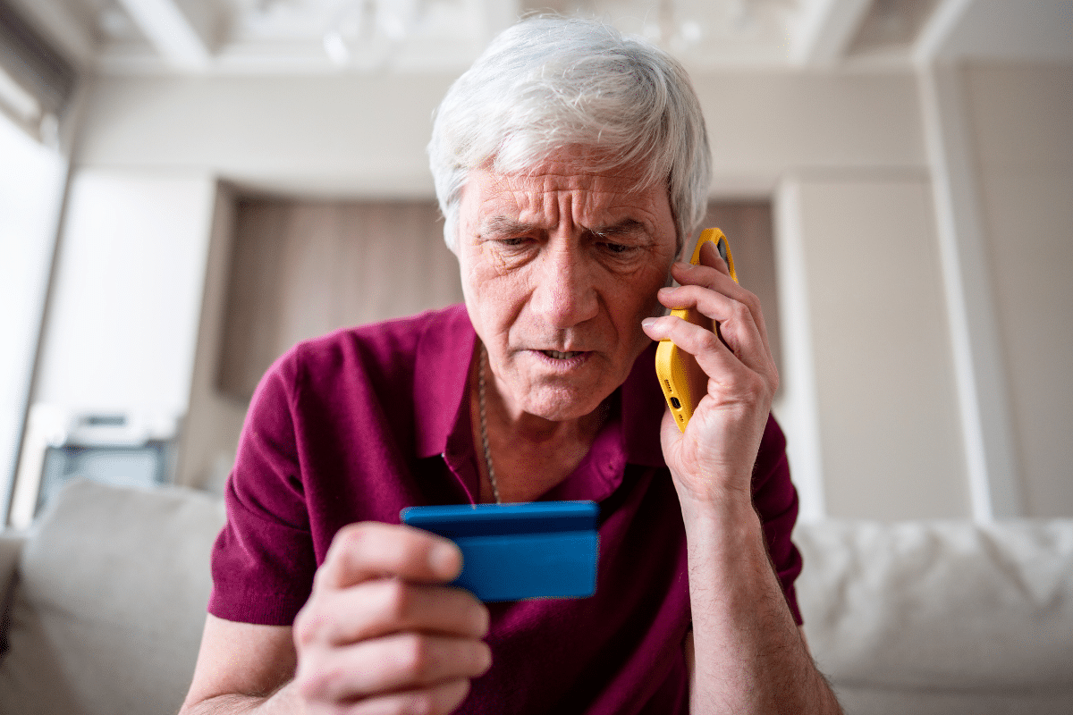 a worried older adult on the phone holding his credit card